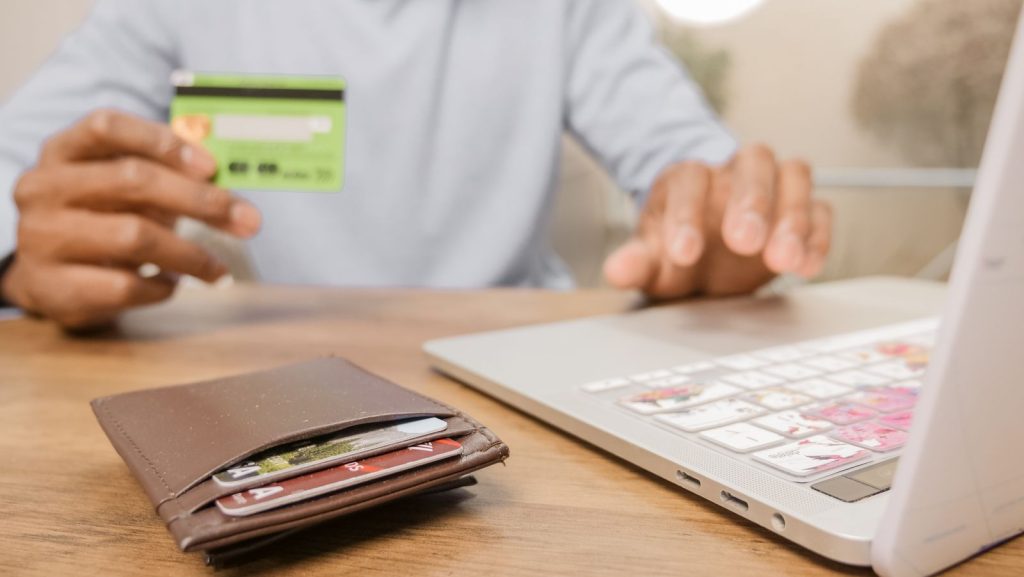 Person holding a bank card next to a laptop, with a wallet of cards on the table