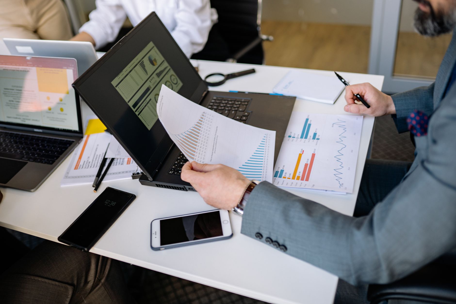 A laptop and mobile phone resting on a desk beside paperwork, suggesting a regulatory review